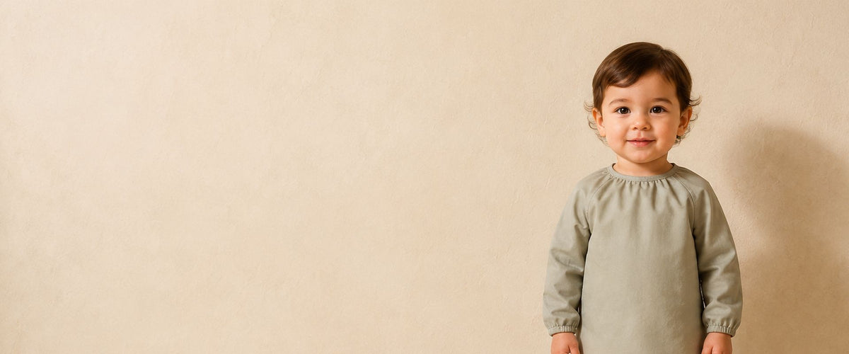 Jeune enfant en blouse tablier vert sauge, à manches longues et encolure froncée.
