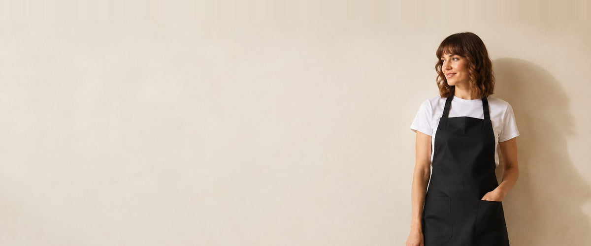 Femme en t-shirt blanc portant un tablier à bavette noir à deux poches basses.