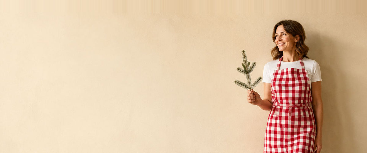 Femme en tablier à bavette à carreaux vichy rouge et blanc, une branche de sapin à la main.
