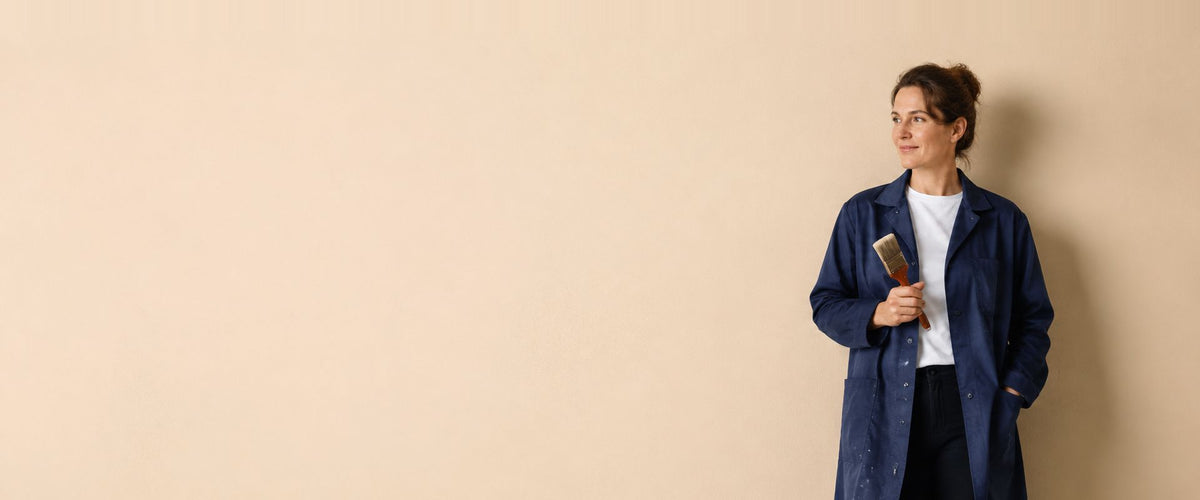 Femme en blouse de travail bleu marine boutonnée, un pinceau plat à la main.