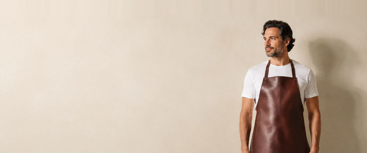 Homme en t-shirt blanc portant un long tablier à bavette brun d'aspect cuir.