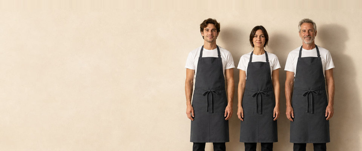 Trois personnes alignées portant le même tablier à bavette gris anthracite noué à la taille.